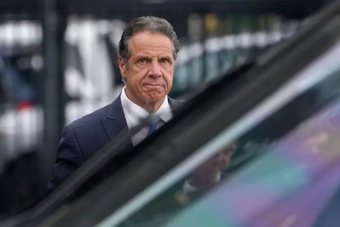 Andrew Cuomo in a blue suit can be seen walking towards a car